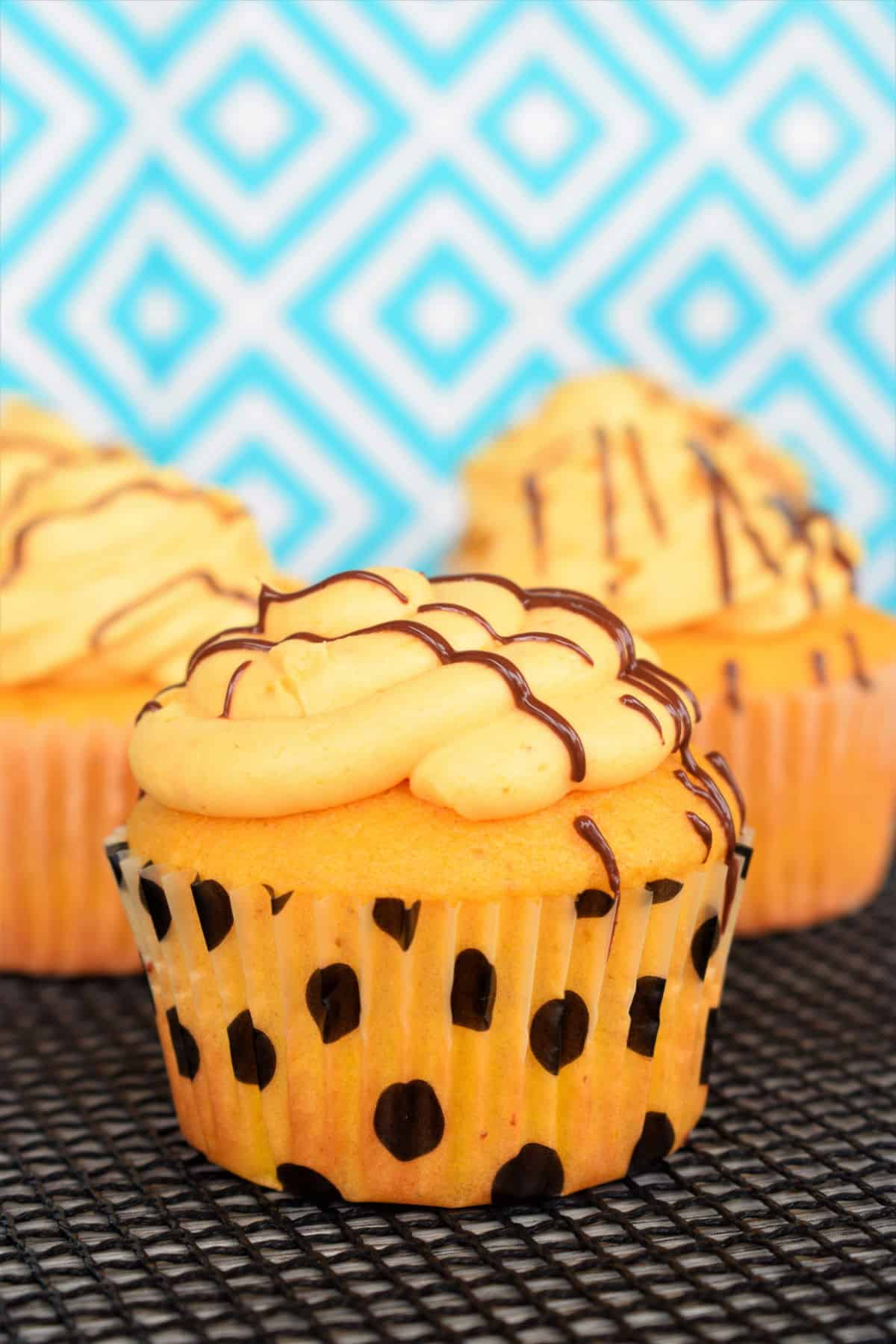 Pumpkin cupcakes with chocolate drizzle on turquoise patterned background.