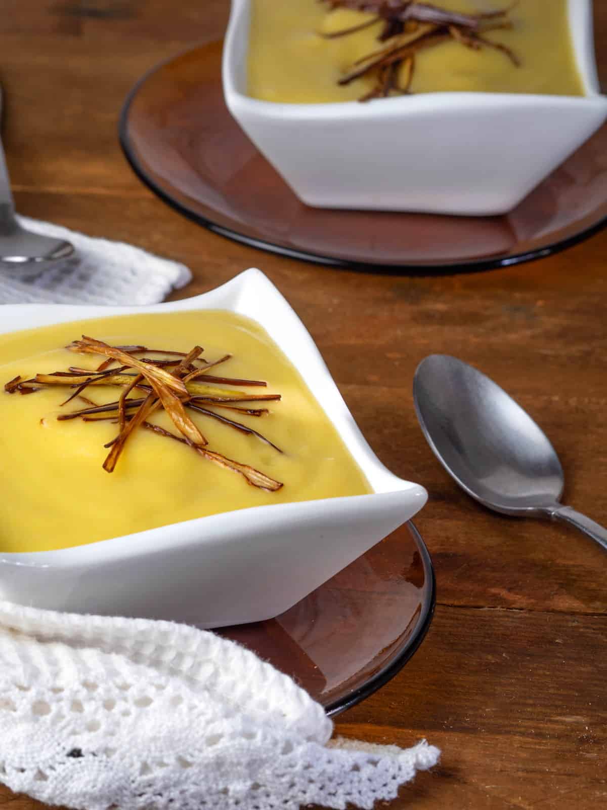 Leek and potato soup in white square soup bowls on wooden background with a spoon on the side.