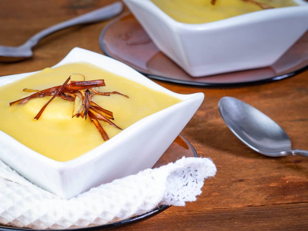 Leek and potato soup in white square soup bowl on wooden background.