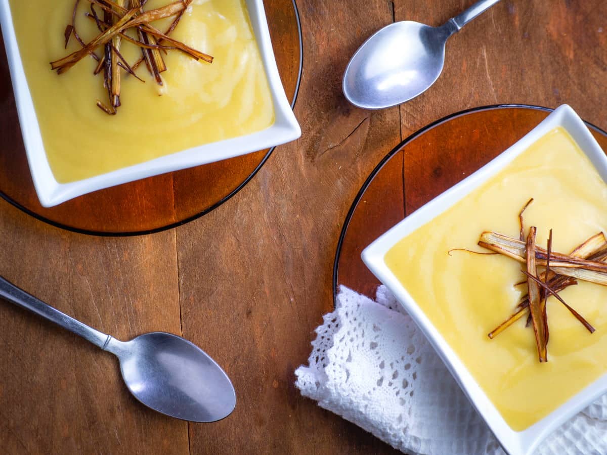 Leek and potato soup in white square soup bowls on wooden background.