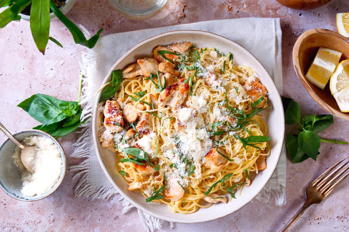 Top view of lemon basil pasta on white plate, lemons and basil on the side.