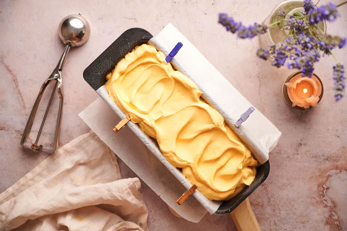 Mac and cheese ice cream in a loaf pan with an ice cream scoop on the side.