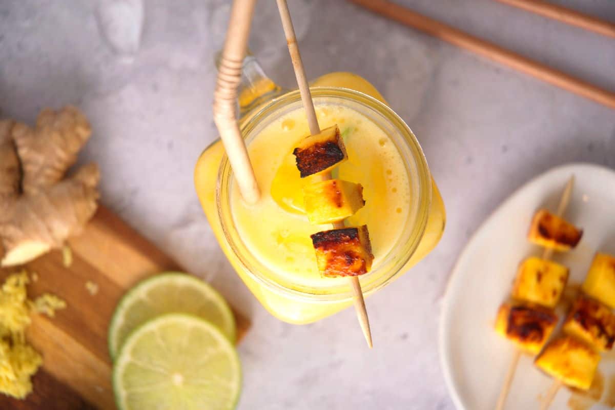 Top view of mango cocktail with grilled mango skewer and a straw in a glass jar.