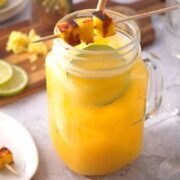Mango cocktail with grilled mango skewer and limes slices in a glass jar.