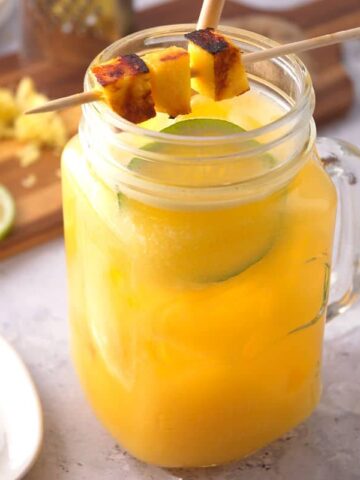 Mango cocktail with grilled mango skewer and limes slices in a glass jar.