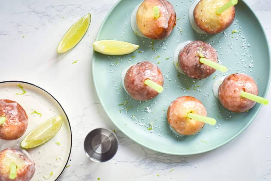 Cake Pop Maker Margarita Cake Pops on a light blue plate with lime wedges and a metal shot glass, marble background.