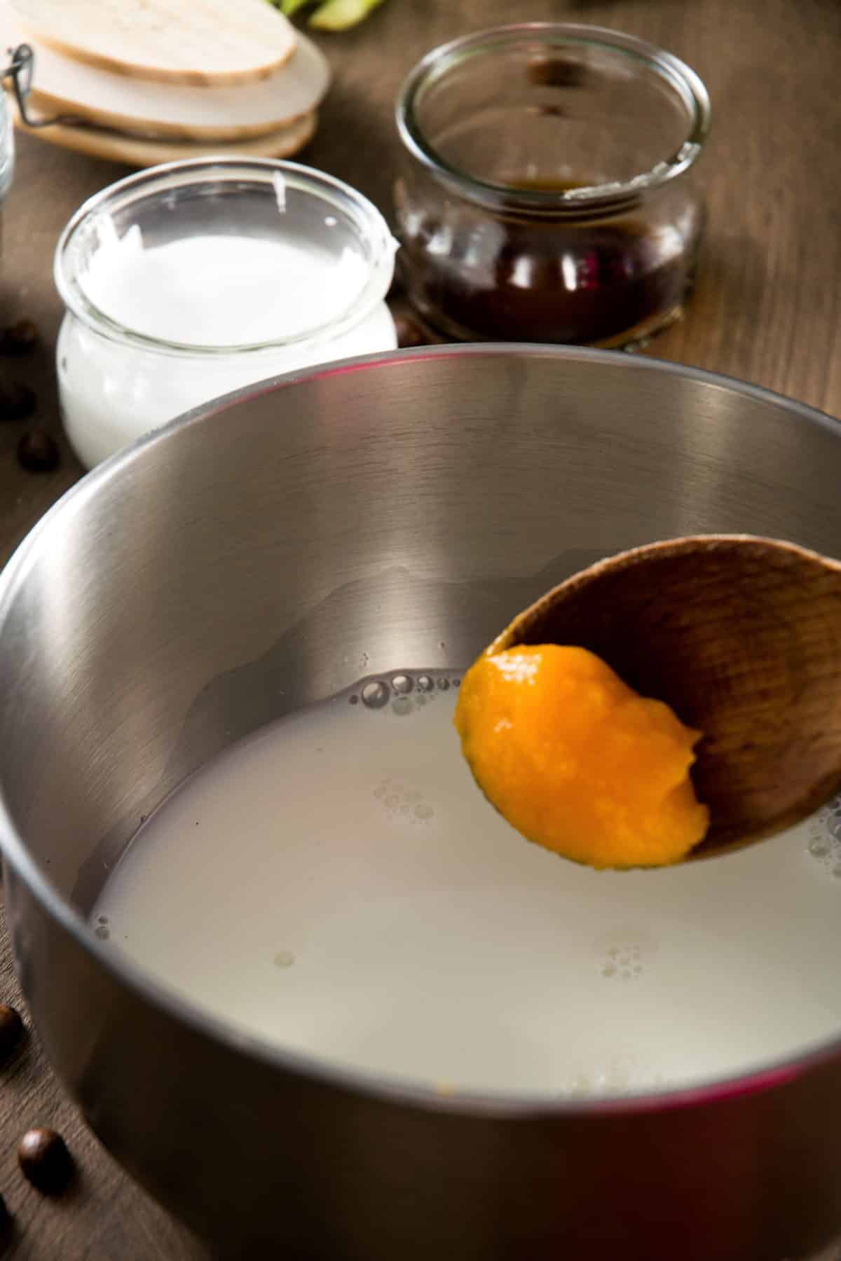 Pumpkin puree on a spoon and milk in a saucepan.