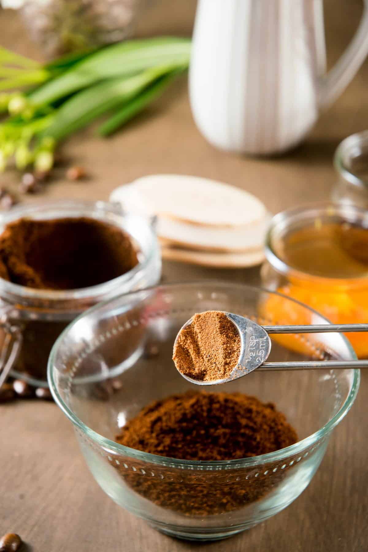 Pumpkin pie spice in a measuring spoon over a small bowl of coffee grind.