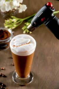 Marshmallow pumpkin latte in a clear glass mug with a kitchen torch.