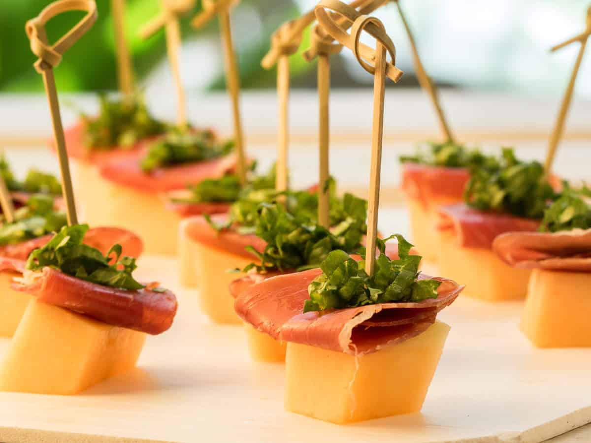 Melon & Prosciutto Skewers with greens on a serving platter.