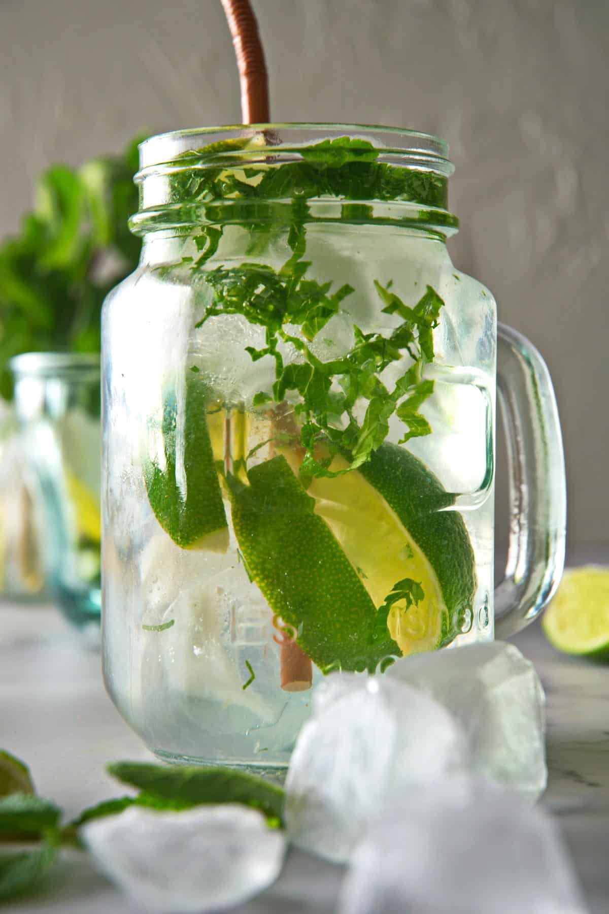 Front view of a mojito mocktail in a glass mug with a brown straw.