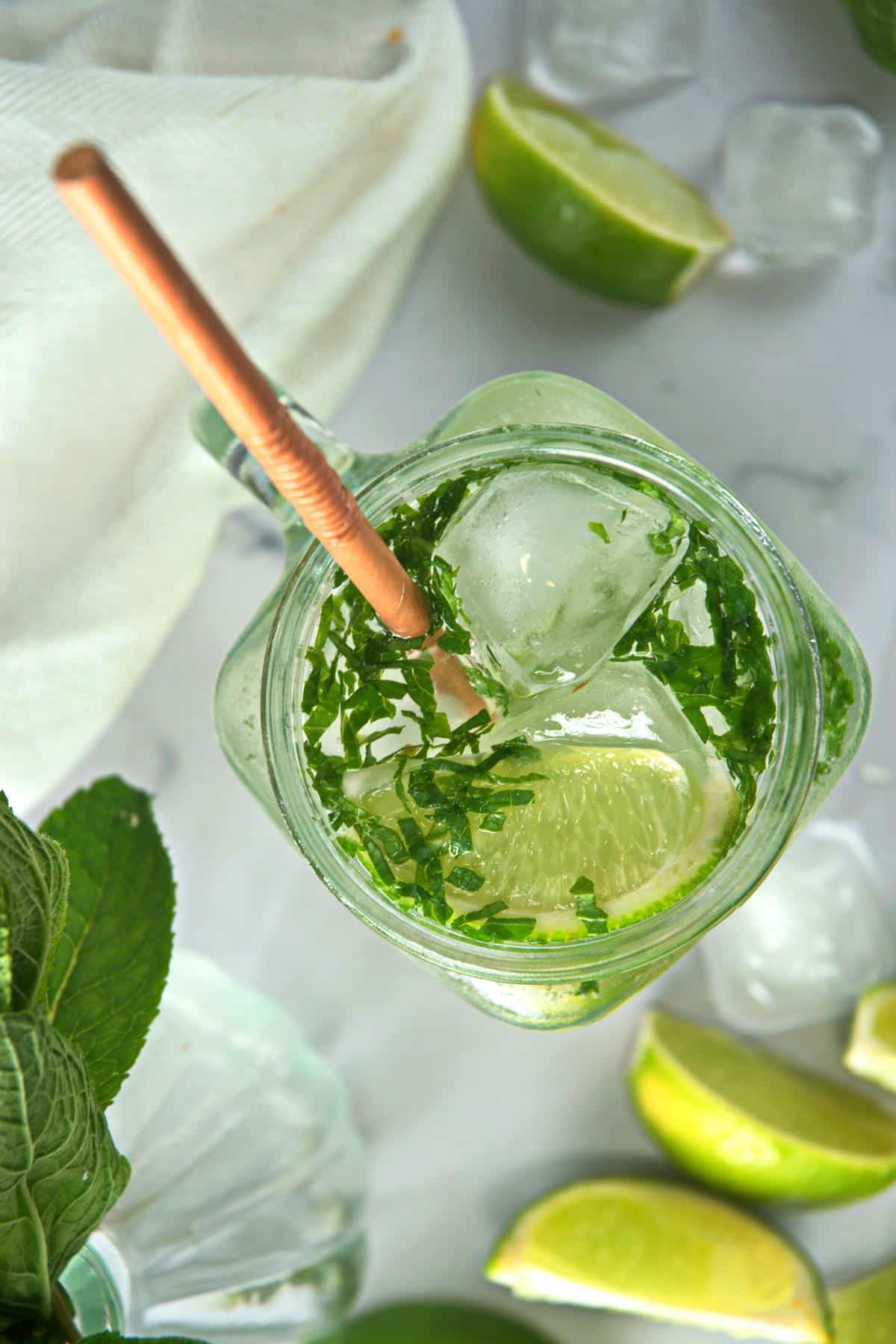 Overhead view of a mojito mocktail in a glass mug with a brown straw and lime wedges on the side.