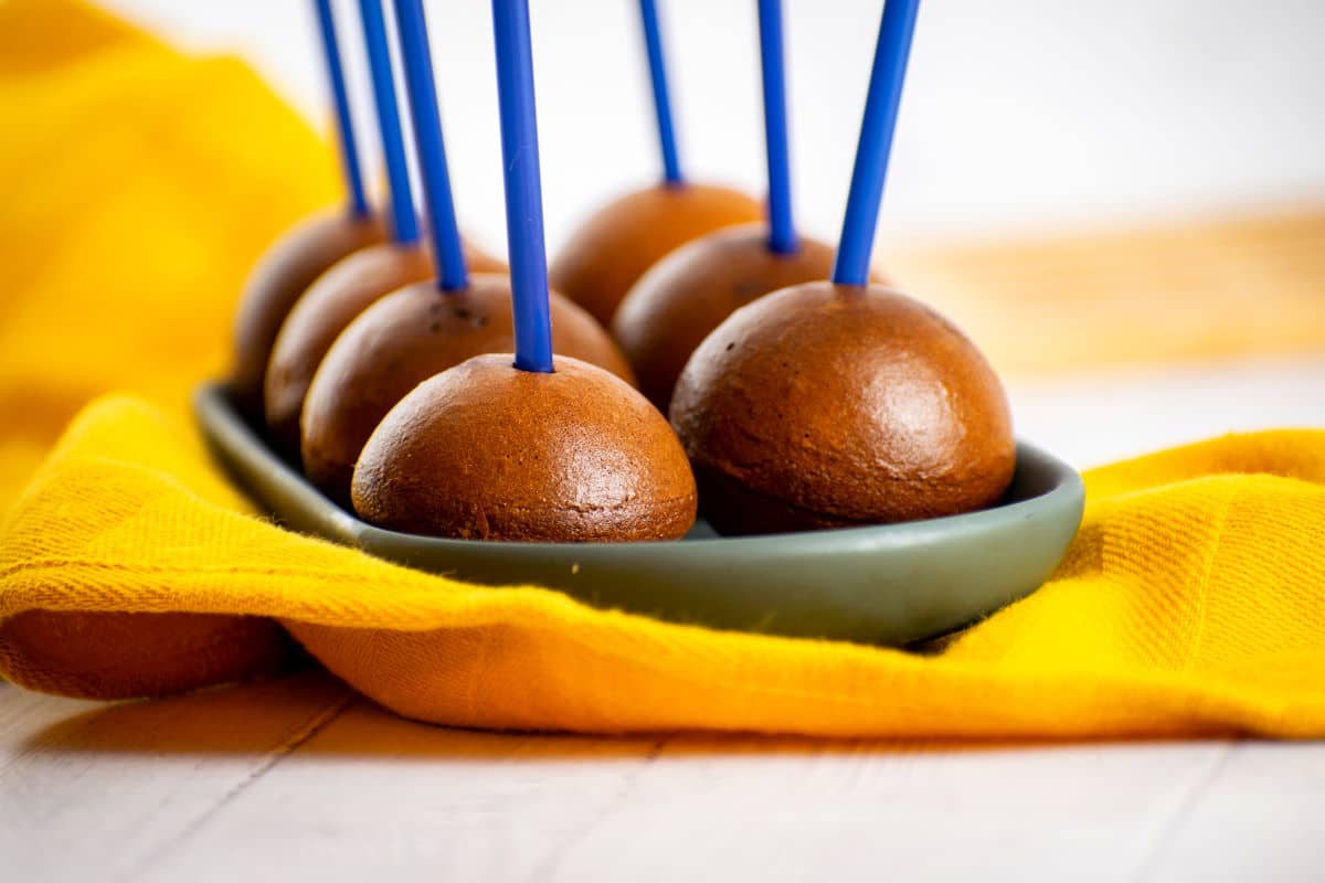 Naked chocolate cake pops on black dish with yellow cloth.