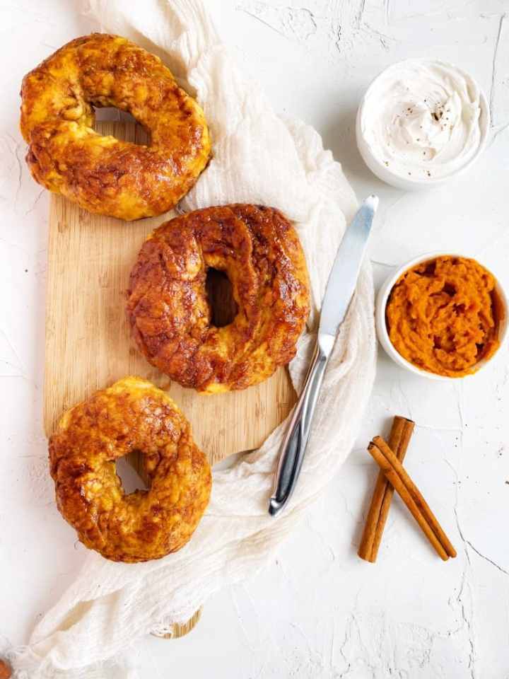 Pumpkin bagels on light background with a butter knife.