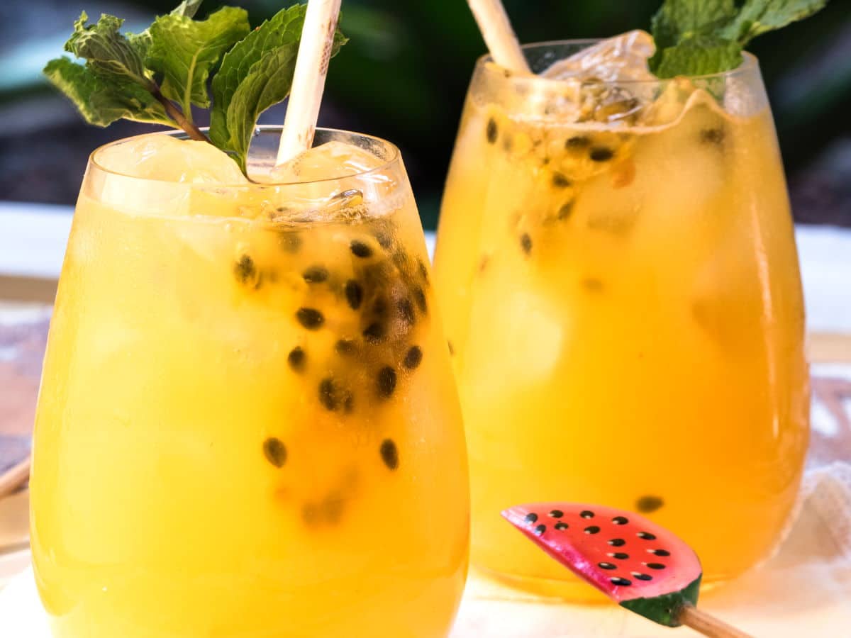 Passion fruit mojitos in 2 wine glasses with mint garnish and paper straws.