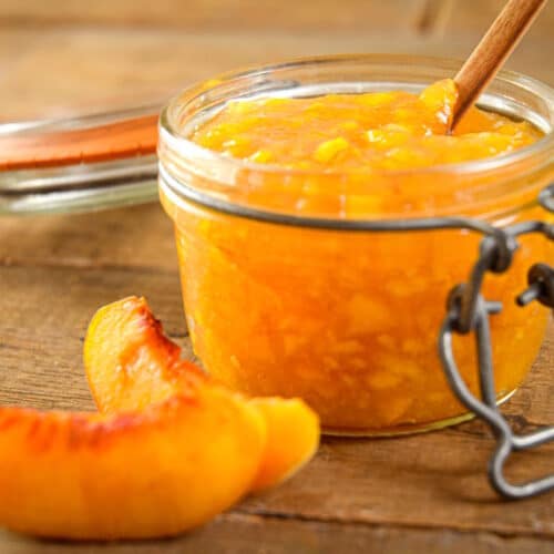 Peach freezer jam in a small jar with fresh peach slices on the side.
