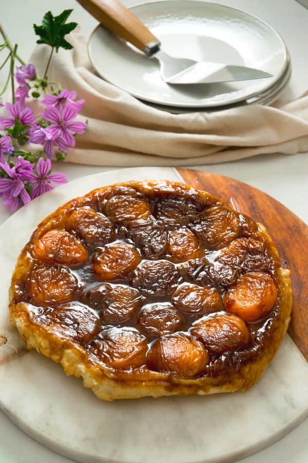 Peach Tarte Tatin on a marble and wooden serving board, purple flowers in the background.
