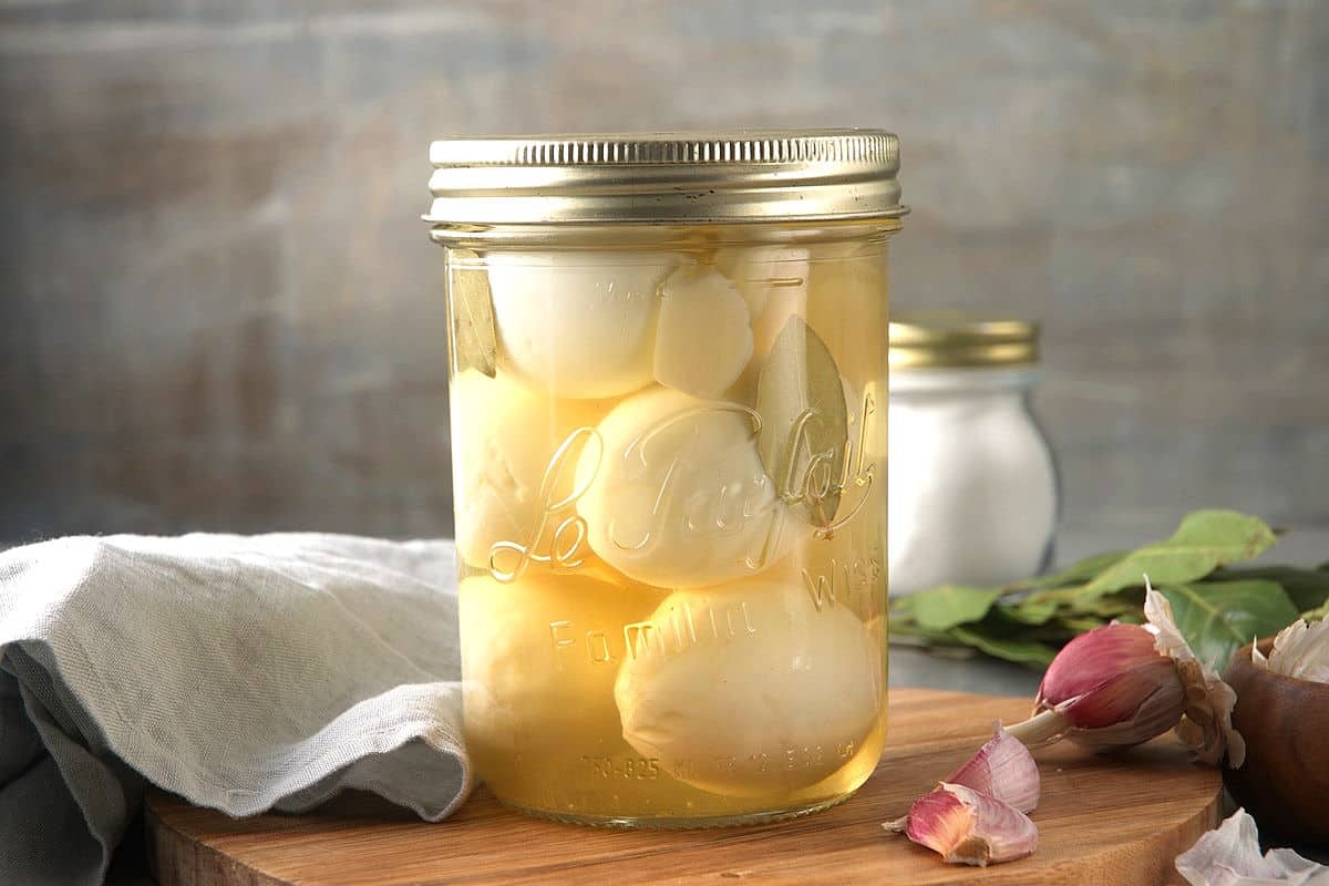 Pickled eggs in a glass jar with garlic cloves on the side.