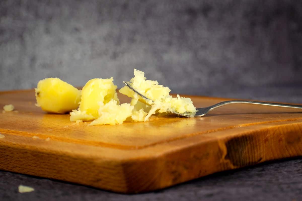 Potato mashed on cutting board with fork.