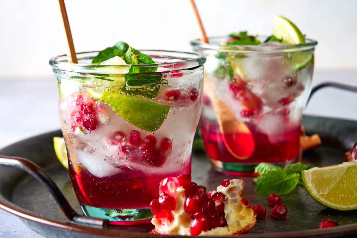 Pomegranate mojito mocktails in glasses on tray.