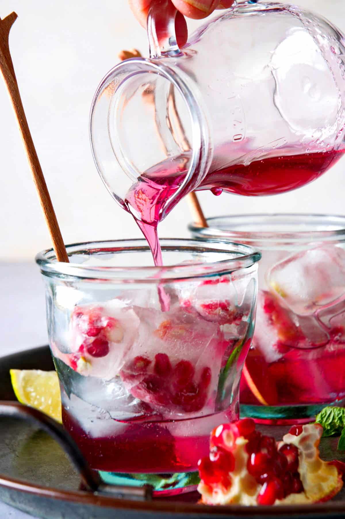 A pitcher of pomegranate syrup pouring into cocktail glass.