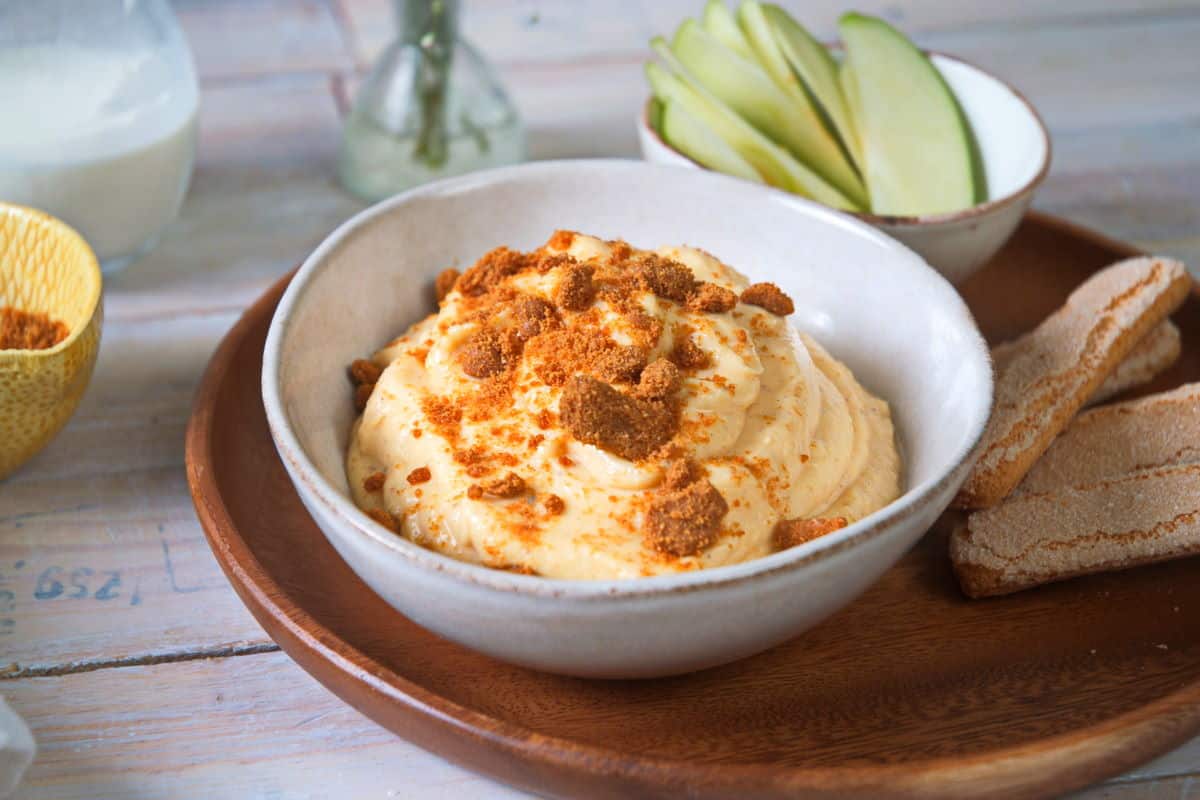 Pumpkin dip in a small bowl with biscuits and apple slices on the side.