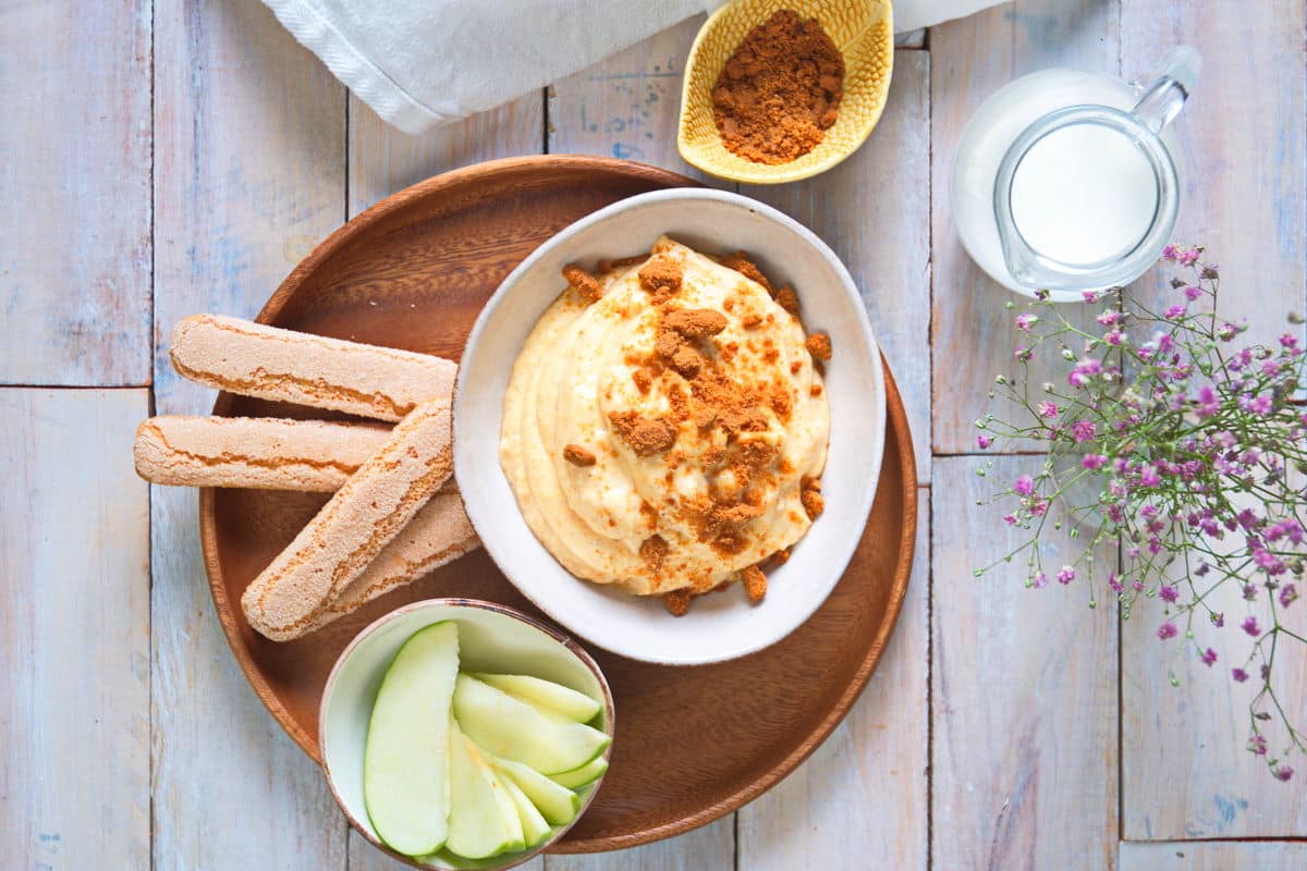 Pumpkin dip in a small bowl with biscuits and apple slices on the side.