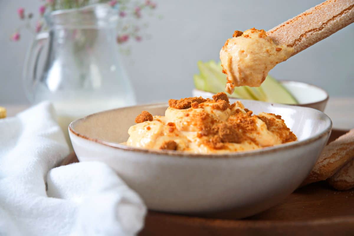 Pumpkin dip with Biscoff cookies crumbled on top and a biscuit dipping into the bowl..