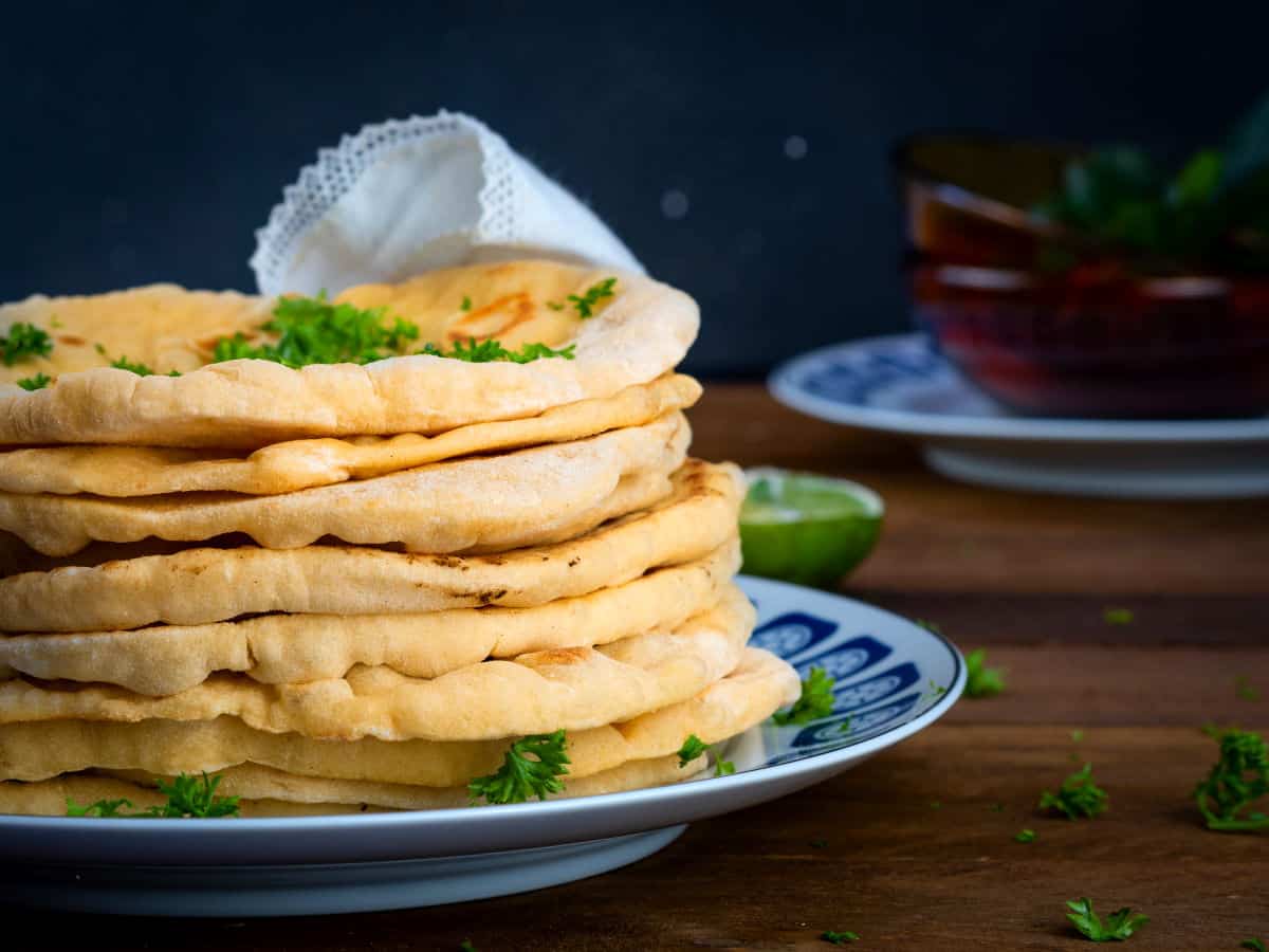 Pumpkin naan bread stacked on a decorative plate with freshly chopped parsley.