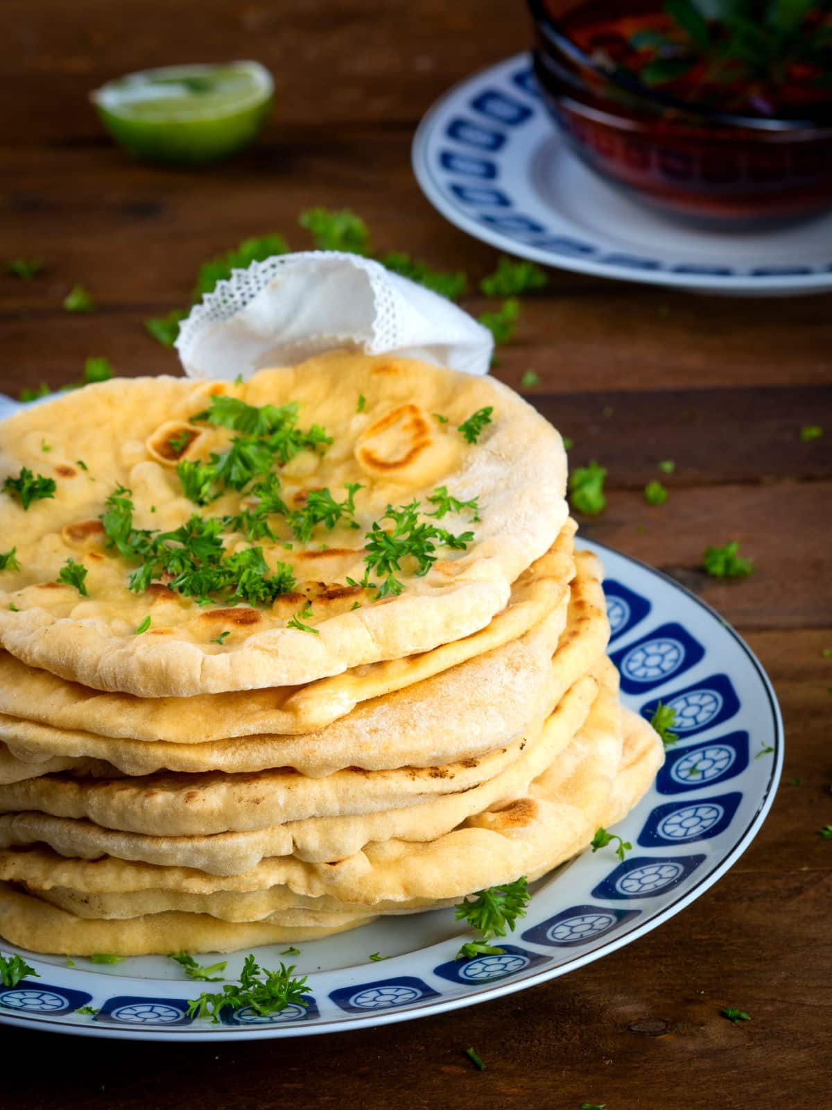 Pumpkin naan bread stacked on a decorative plate with freshly chopped parsley.