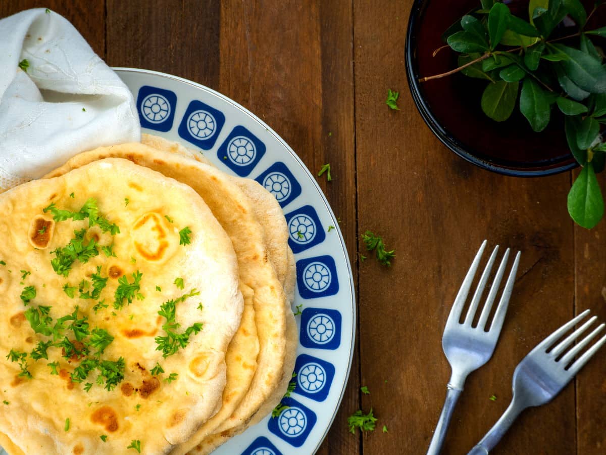 Top view of pumpkin naan bread stacked on a decorative plate with a plant and forks on the side.