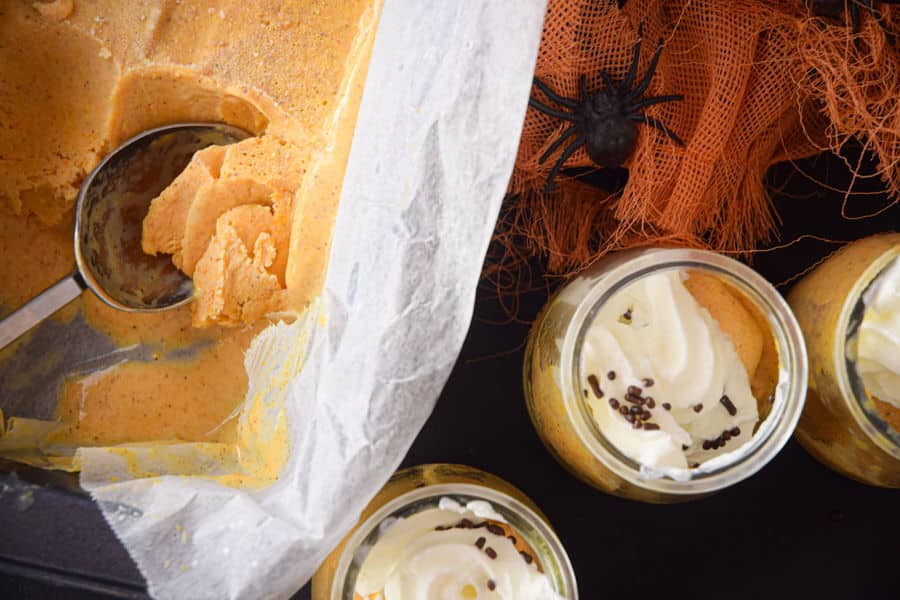 Pumpkin spice ice cream in small glass jars with orange fabric and plastic spiders.