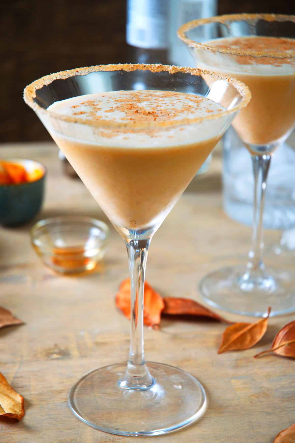 Pumpkin cocktail in martini glasses and orange leaves scattered around the drinks.