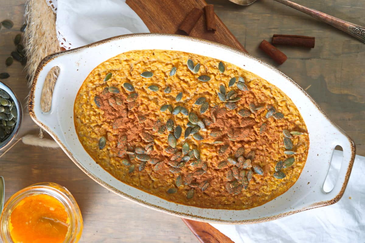 Top view of pumpkin spice oatmeal in a white casserole dish on wooden cutting board.