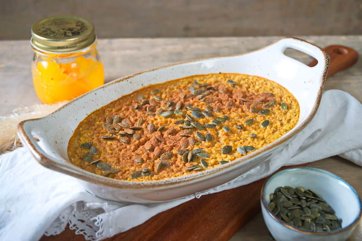 Pumpkin spice oatmeal in a white casserole dish on wooden cutting board.