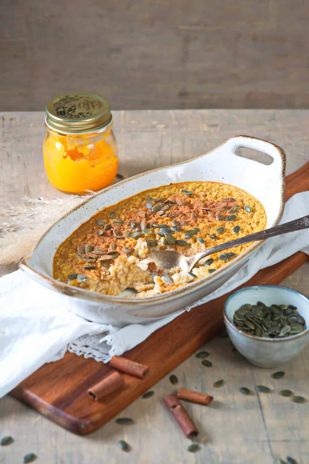 Pumpkin spice oatmeal in a white casserole dish on wooden cutting board.