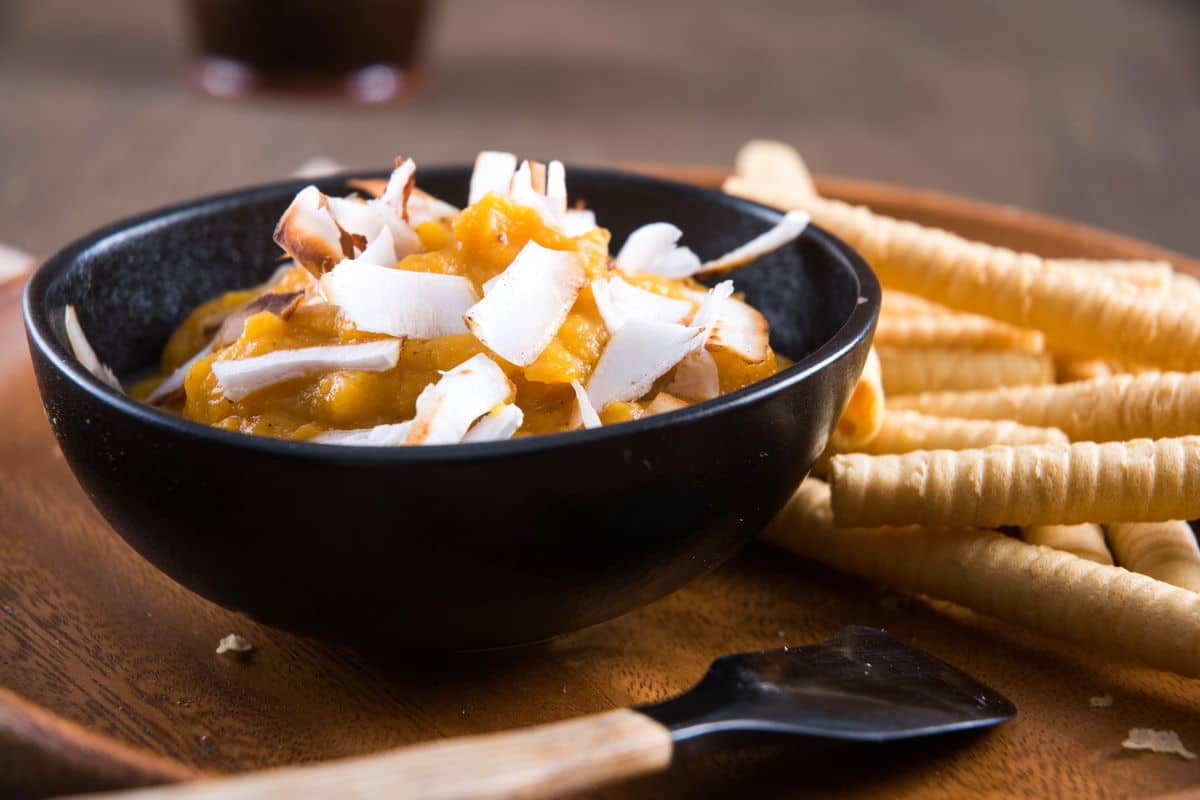 Pumpkin pie hummus in a bowl with toasted coconut flake topping, breadsticks on the side.