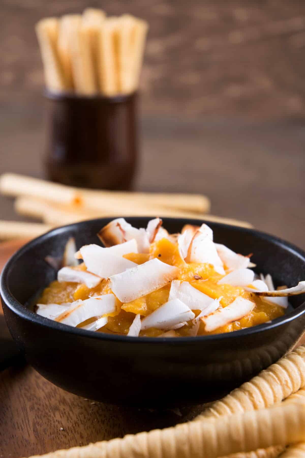 Pumpkin pie hummus in a bowl with toasted coconut flake topping, breadsticks on the side.