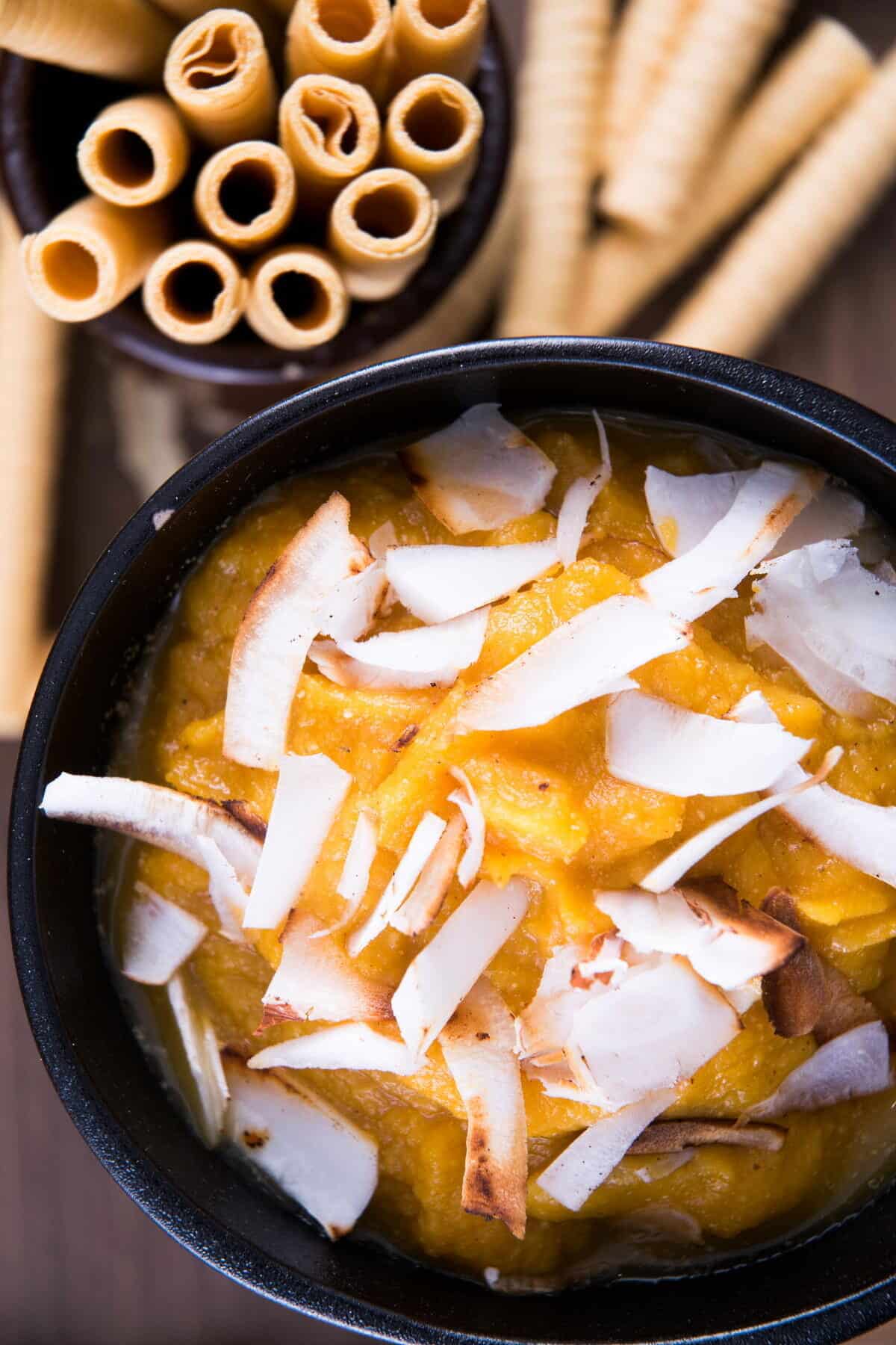 Pumpkin pie hummus in a black bowl with toasted coconut flake topping, breadsticks on the side.