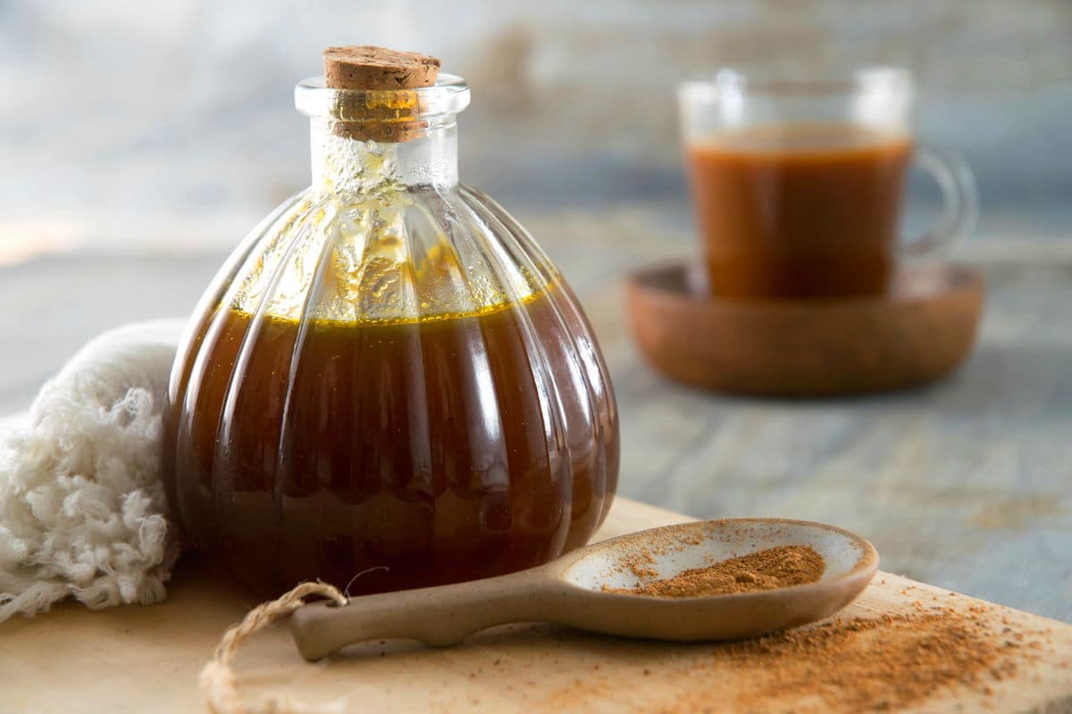 Pumpkin spice syrup in a small decorative jar, a spoon of pumpkin pie spice and a glass of pumpkin spice latte on the side.