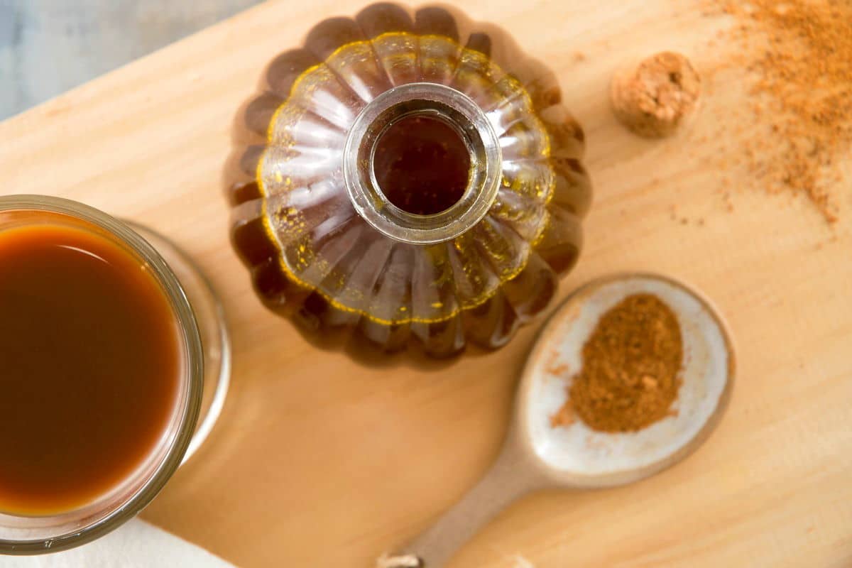 Pumpkin spice syrup in a small decorative jar, a spoon of pumpkin pie spice and a glass of pumpkin spice latte on the side.