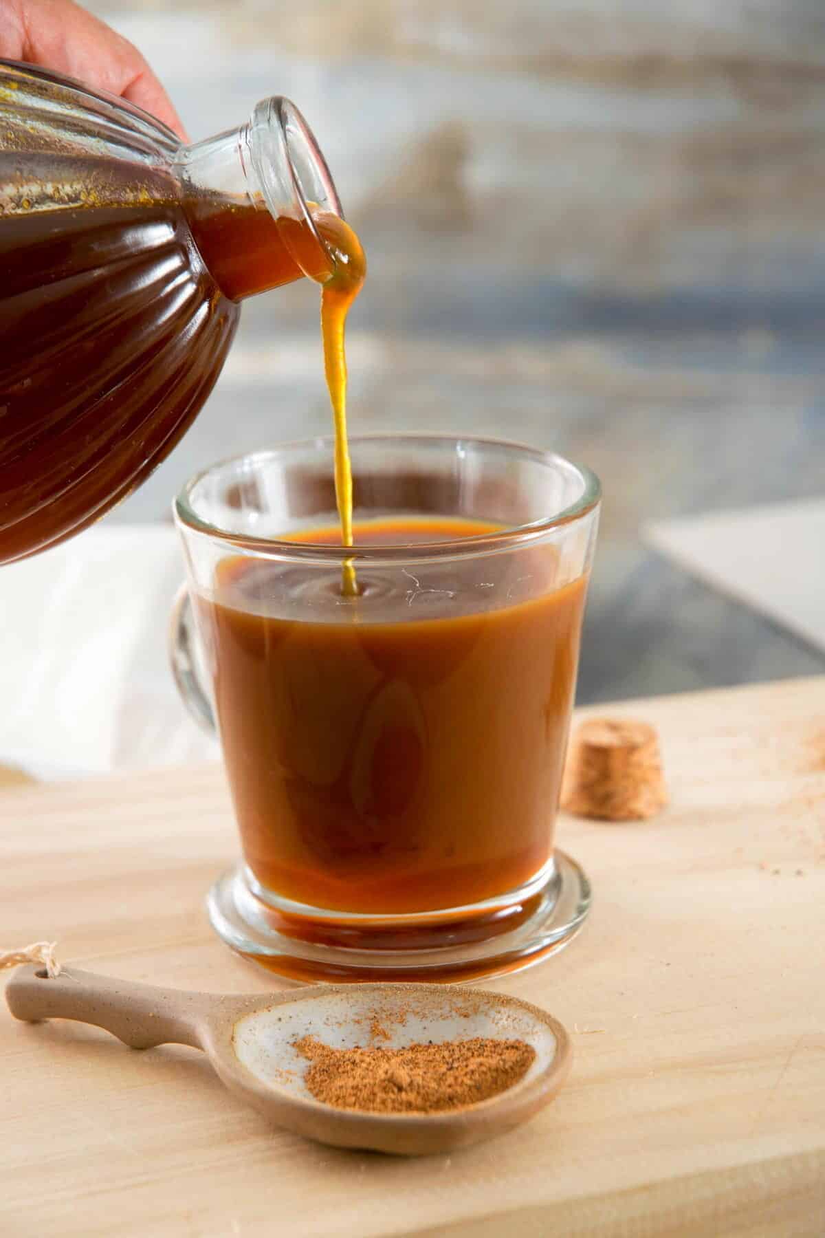 Pumpkin spice syrup pouring into a clear, glass mug of coffee.