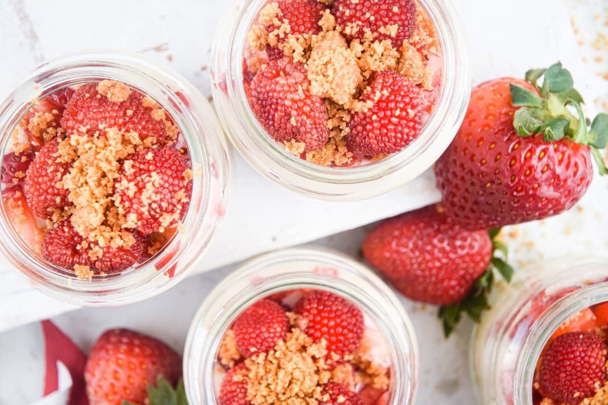 Raspberry cheesecake in mini dessert jars, top view, with strawberries around the jars.