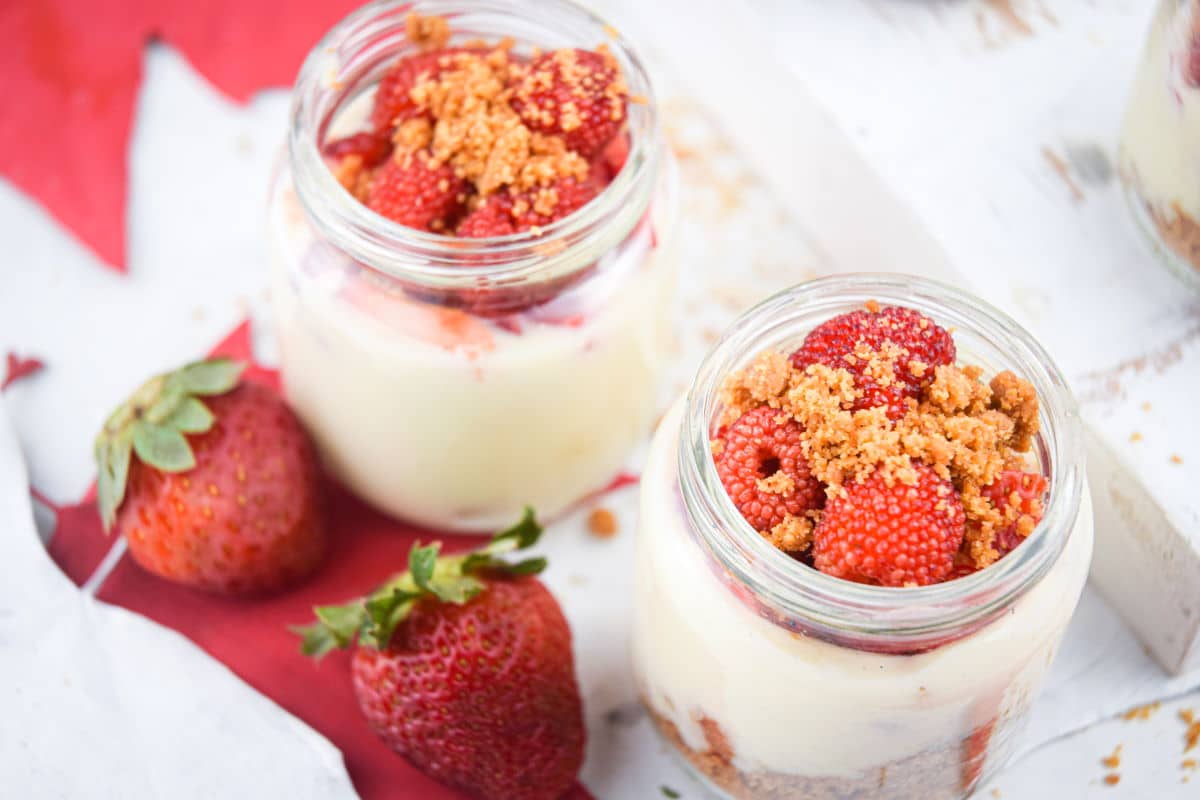 Raspberry cheesecake in mini dessert jars with strawberries on the side.