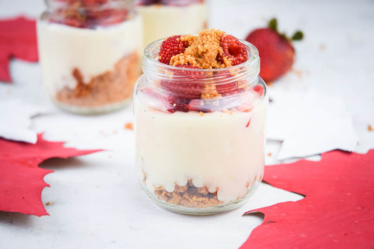 Raspberry cheesecake in mini dessert jar on white background with maple leaves.