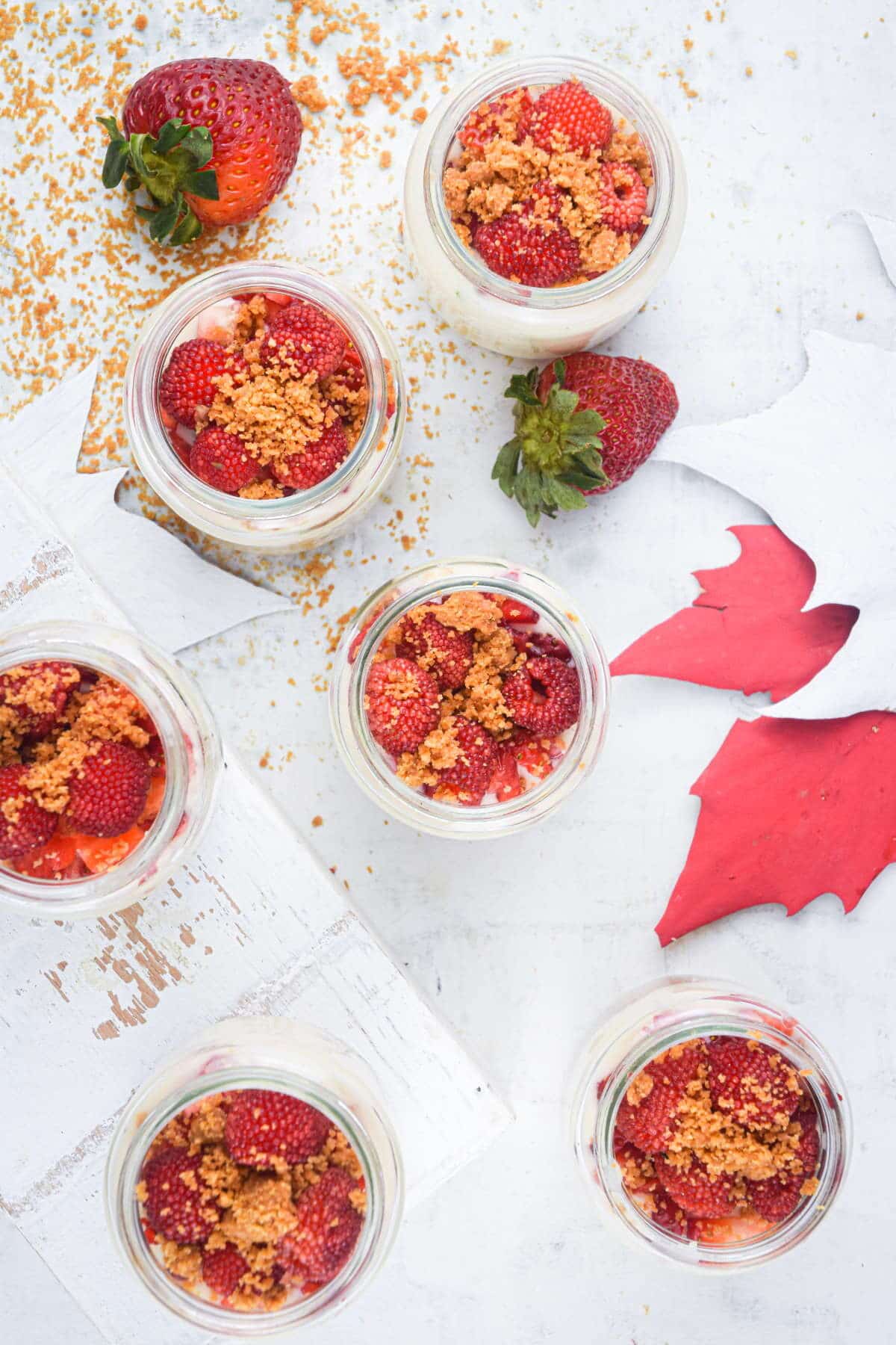 Top view of raspberry cheesecake in mini dessert jars, maple leaves in the background.