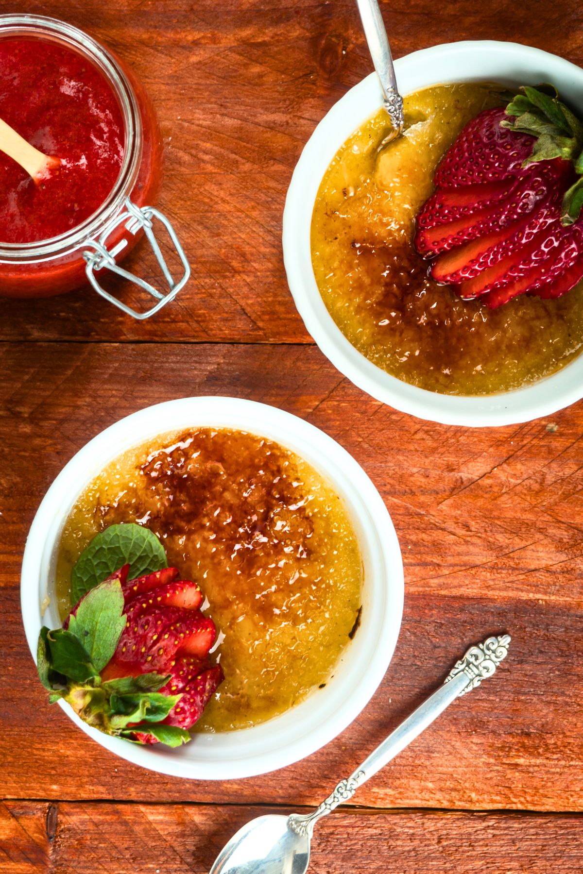 Raspberry Coulis Crème Brûlée in ramekins with spoons on wooden background.