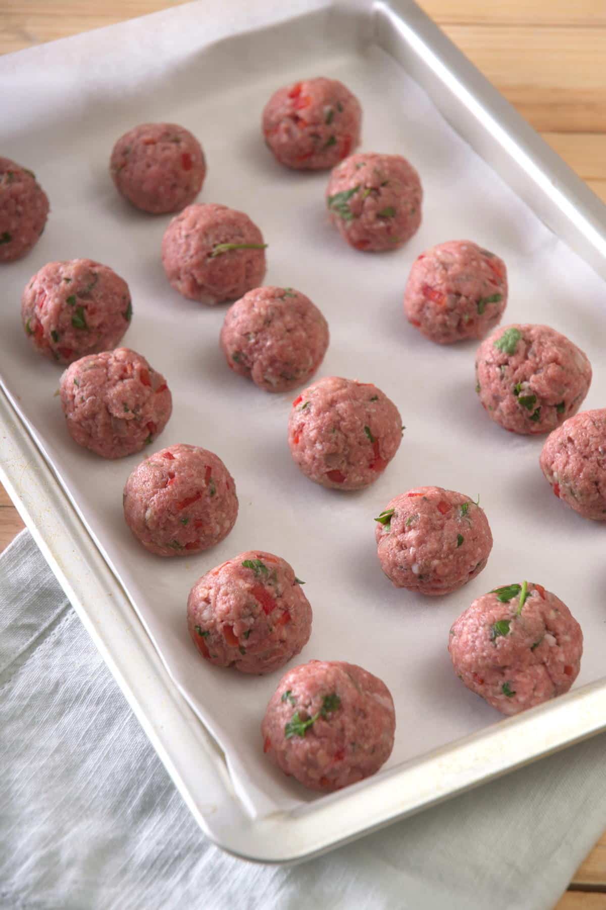 Raw bison meatballs on parchment lined baking sheet.