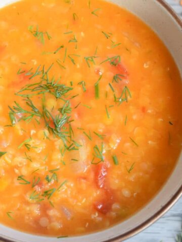 Top view of red lentil soup in a bowl, grey wood background.