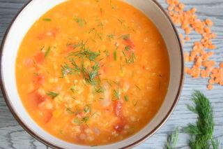 Red lentil dill soup in a bowl, wooden background, dill and lentils on the side.